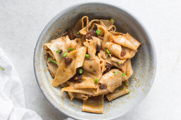 Overhead view of spicy wide noodles in a grey bowl, top view of biangbiang mian in a bowl, spicy belt noodles with green onions and diced pork in a bowl