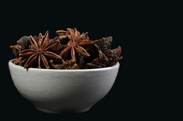 Star anise in a white bowl on a black background, close-up photo of star anise, isolated stock photography