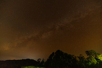 Fototapeta premium Time lapse Milky Way above mountains at night in autumn. Landscape with mountain valley, low clouds, purple starry sky with milky way. The Milky Way shines on a cold night in the north of Thailand