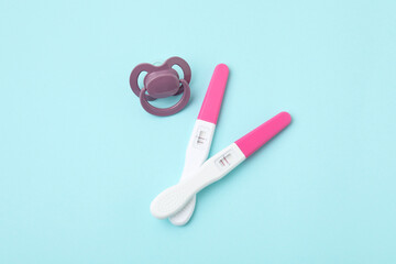 Pregnancy tests and pacifier on light blue background