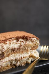 Piece of tasty tiramisu and fork on black table, closeup