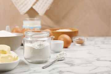 Baking powder in jar and other products on white marble table, closeup. Space for text