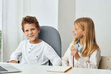 Obraz premium Happy children studying together at home with their laptops and headphones The boy and girl are sitting at a table in the cozy living room, completely focused on their online learning The room is