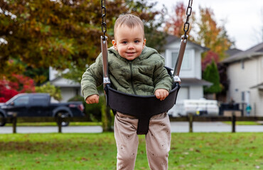 Happy Toddler Enjoying Swing In Autumn Neighborhood Park