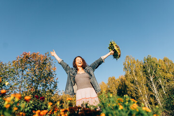 Smiling woman with curly hair holding a sunflower, radiating happiness and positivity. Woman celebrating the harvest festival, holding a sunflower on her rural farm with a smile