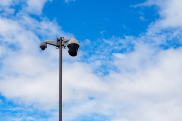 Security Camera on a Pole Against a Bright Blue Sky with White Clouds, Illustrating Surveillance Technology and Outdoor Safety Measures