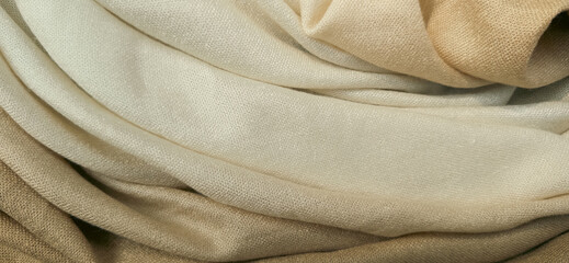 Close-up photograph showcasing the soft texture and folds of a beige and brown fabric. Premium...