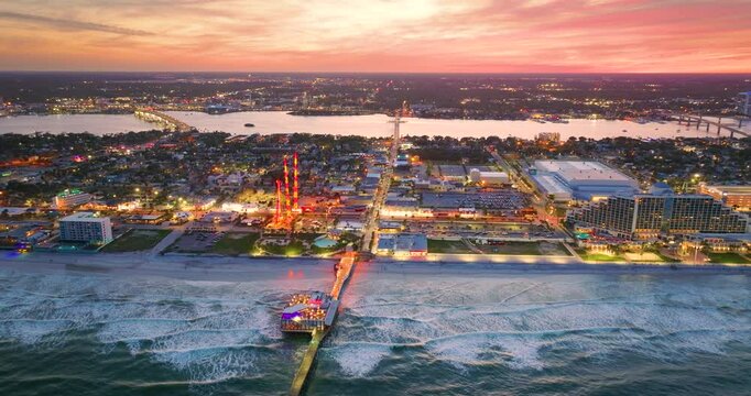 Tourist attractions on American southern seashore in Daytona Beach city, Florida at sunset. Illuminated Main Street Pier and Breakers Oceanfront Park. Luxurious hotels and apartment buildings.