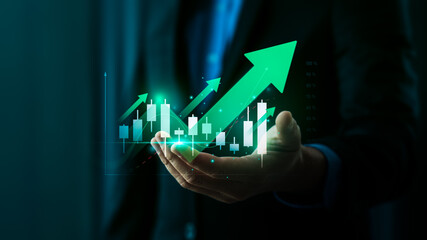 Businessman's Hand Holding Holographic Stock Market Growth Chart with Green Arrow Showing Positive Financial Trends and Stock Candlestick Data on Digital Interface and Finance