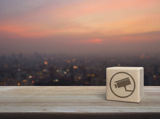 Cctv camera icon on wood block cube on wooden table over blur of cityscape on warm light sundown, Technology security and safety online concept