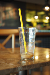 An Empty Glass Featuring a Yellow Straw is Placed on a Rustic Table Inside the Cafe