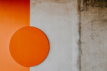 A vivid orange circle is positioned on a textured gray wall, complemented by a bold orange section