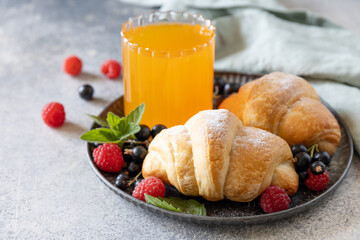 Tasty freshly baked croissants and orange juice on a grey stone background, breakfast concept.