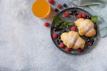 Tasty freshly baked croissants and orange juice on a grey stone background, breakfast concept.