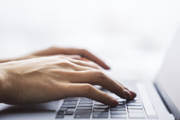 Female hands typing on a trendy laptop keyboard, with a blurry office scene in the background