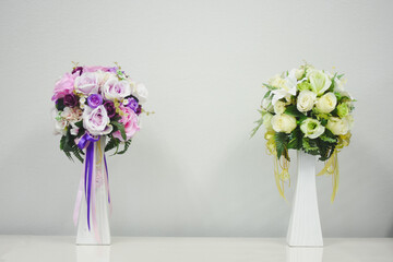 two floral arrangements in white vases. The arrangement on the left consists of various shades of...