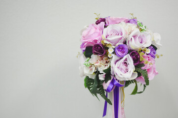 The bouquet consists of various flowers, predominantly roses, in shades of pink, purple, and white. There are also some small white flowers and green leaves interspersed among the roses.