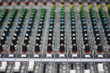 close-up view of an audio mixing console. The console features multiple rows of knobs and sliders.