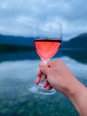 Hand holding a glass of wine with mountain and lake views at the background. Person holding a glass of wine