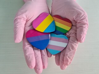 Colorful heart-shaped tokens representing varied pride flags held in pink-gloved