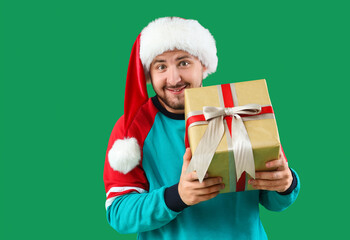 Young man in Santa hat with gift box on green background