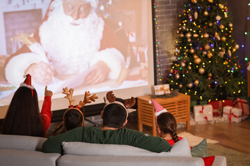 Happy family watching Christmas movie on projector screen at home, back view