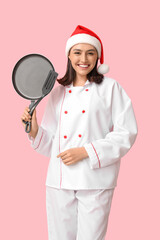 Beautiful female chef in Santa hat with frying pan and spatula on pink background