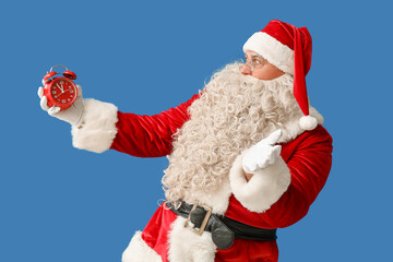 Surprised Santa Claus with alarm clock on blue background