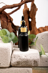 Naklejka premium Matte Black Dropper Bottles on Stone Blocks with Greenery for Natural Skincare Branding
