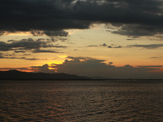 Obraz premium Sunset over the lake with clouds and mountains in the background.