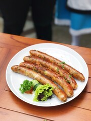 4 Long beef sausages with veggies on white plate at the top of wooden table. Suits for restaurant menu design, recipe, and food projects