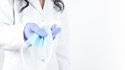 Close-up of doctors hand holding a medical face mask, on white background