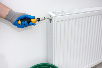 A plumber uses a tool to drain air, draining water and air from a radiator in an apartment.