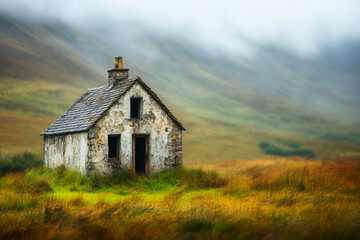 Rustic Abandoned House in a Lush Green Field Surrounded by Misty Mountains Perfect for Evoking Feelings of Nostalgia and Solitude in Nature Photography