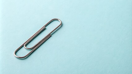 A single silver paperclip rests on a smooth, pale blue surface, a simple yet poignant image of organization and connection.