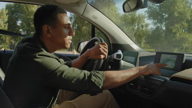 Portrait of attractive African American male driver sitting in car searching for travel route on trip computer , using modern GPS navigation system while driving vehicle on road trip.