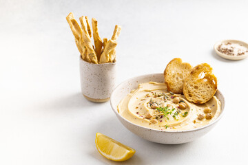 Hummus with olive oil in a gray ceramic plate. Toast and breadsticks for snacks.