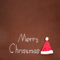 Merry Christmas handwritten in chalk, with Santa's hat nearby, on an abstract background, With space for text