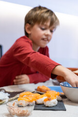 School age boy preparing sushi at home with different ingredients