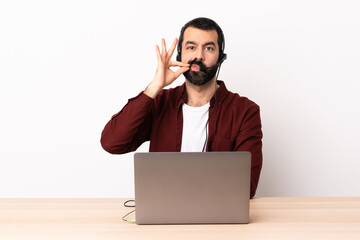 Telemarketer caucasian man working with a headset and with laptop showing a sign of silence gesture.