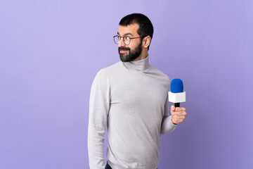 Adult reporter man with beard holding a microphone over isolated purple background . Portrait