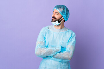 Surgeon man with beard with blue uniform over isolated purple background having doubts while...