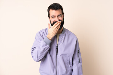 Caucasian man with beard wearing a jacket over isolated background happy and smiling covering mouth with hand