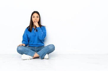 Young mixed race woman sitting on the floor isolated on white background surprised and shocked while looking right