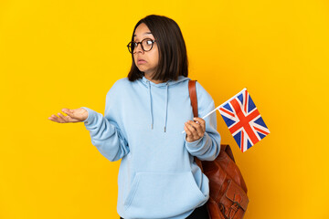 Young latin woman holding an United Kingdom flag isolated on yellow background with surprise expression while looking side