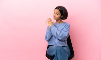 Young mixed race woman sitting on a chair isolated on pink background scheming something