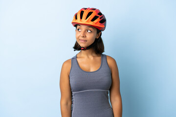 Young cyclist woman isolated on blue background having doubts while looking side
