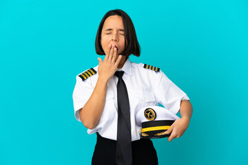Young airplane pilot over isolated blue background yawning and covering wide open mouth with hand