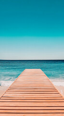 Fototapeta premium A wooden pier extends out into the blue ocean on a bright, sunny day. The water is calm and clear, with a slight wave lapping at the shore