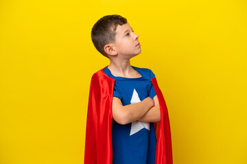 Little caucasian boy isolated on yellow background in superhero costume with arms crossed